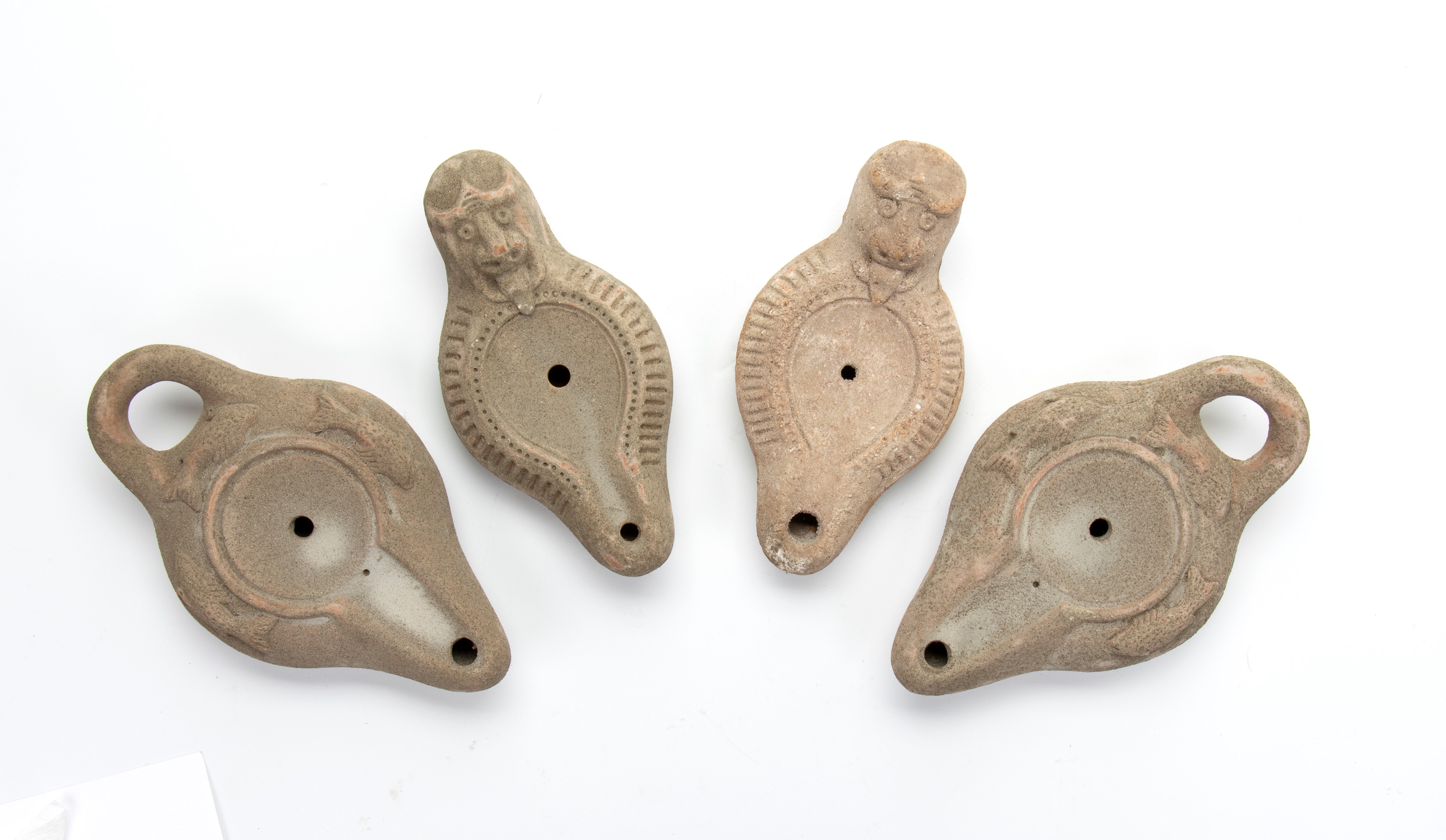 Lotto di quattro lucerne in terracotta, due con mascherone e 2 con pesci a rilievo