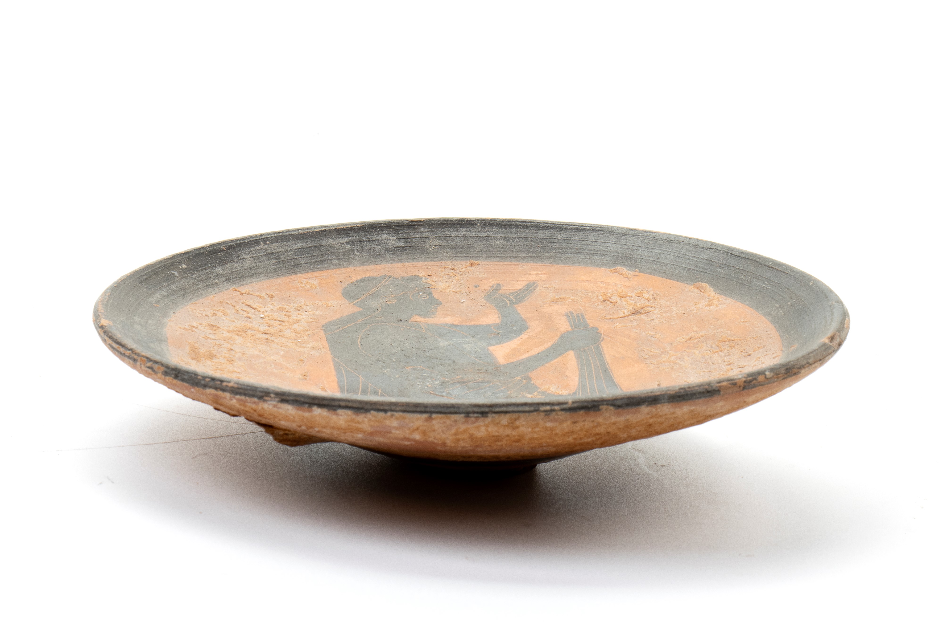 Piattino in ceramica arcaica a figure nere decorato con figura stante a sorreggere un panneggio