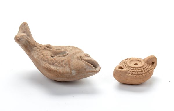 Lotto di due lucerne in terracotta, una a forma di pesce con ancora e defino a rilievo, l'altra con decoro a rilievo a rete