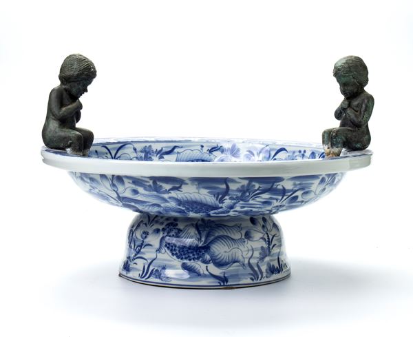 Centrotavola in ceramica smaltata nei toni del bianco e blu con applicazione di due putti a imitazione di fontana