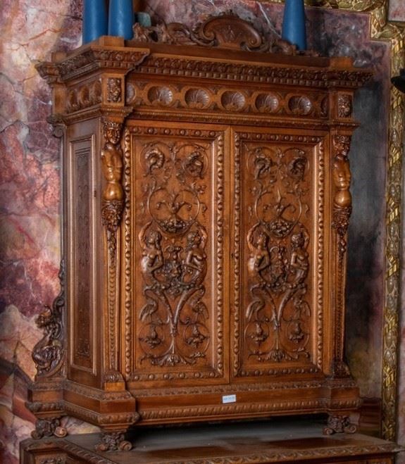 Mobile credenza a doppio sportello in noce con piedi a mensola e mascheroni; grifi laterali. Agli sportelli preziosa lavorazione a grottesche con candelabre e nudi femminili di ispirazione mitologica. Unghiature alla cornice inferire