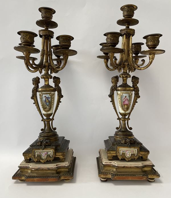 Coppia di candelabri a cinque fuochi in bronzo dorato finemente cesellato con figure muliebri a rilievo e con inserti in porcellana raffiguranti giovin signore e giovin signora al fusto. Base quadrata mistilinea. 