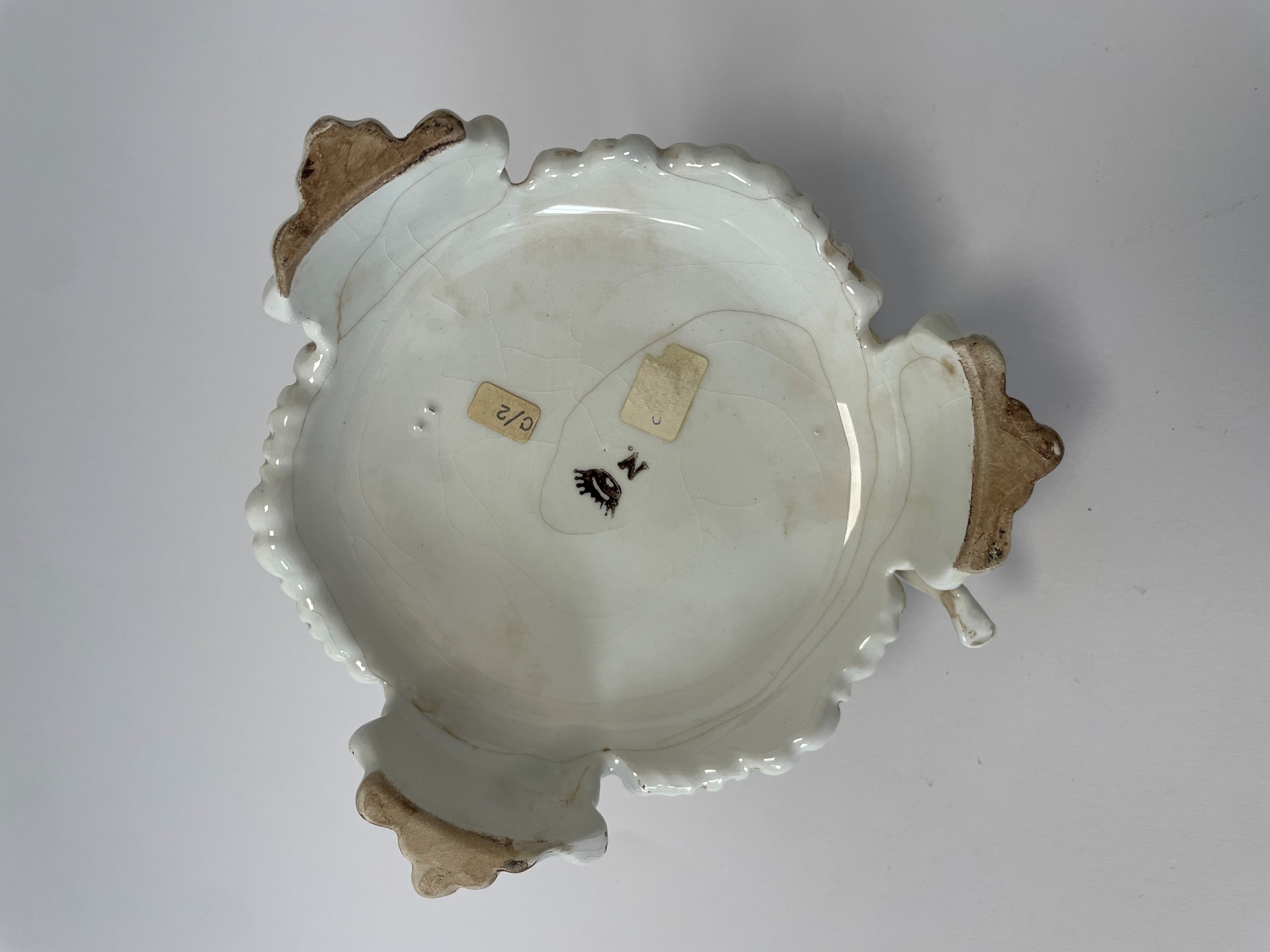 Composizione in porcellana bianca con inserti policromi di fiori raffigurante tre putti che suona...