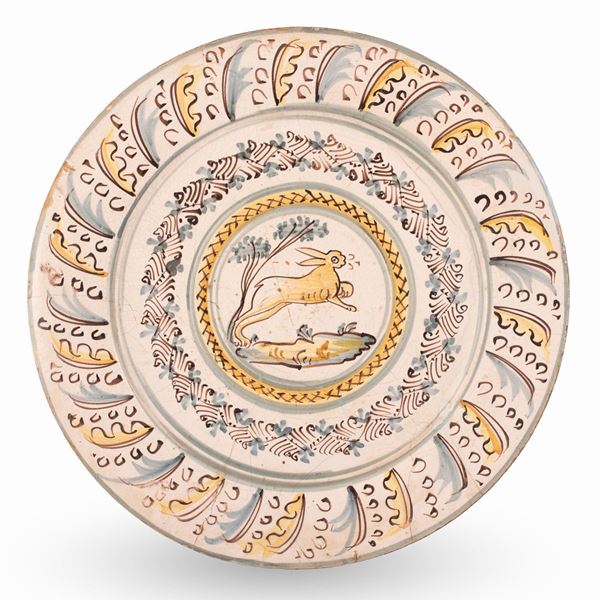 Manifattura di Bussi sul Tirino del XVII secolo - Maiolica a gran fuoco decorata nello stile compendiario, tesa con piume di struzzo stilizzate nei toni del blu e giallo, cavetto con decoro vegetale e lepre in fuga in un paesaggio. 