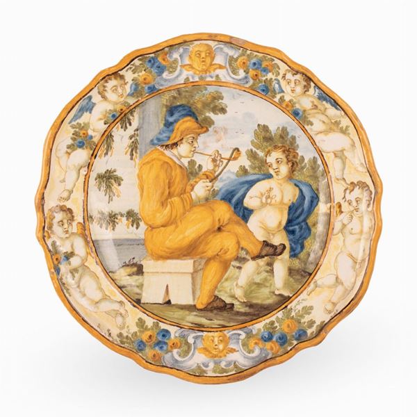Manifattura castellana del XVIII secolo - Piatto in maiolica decorato al cavetto con scena istoriata di fumatore di pipa e putto. 