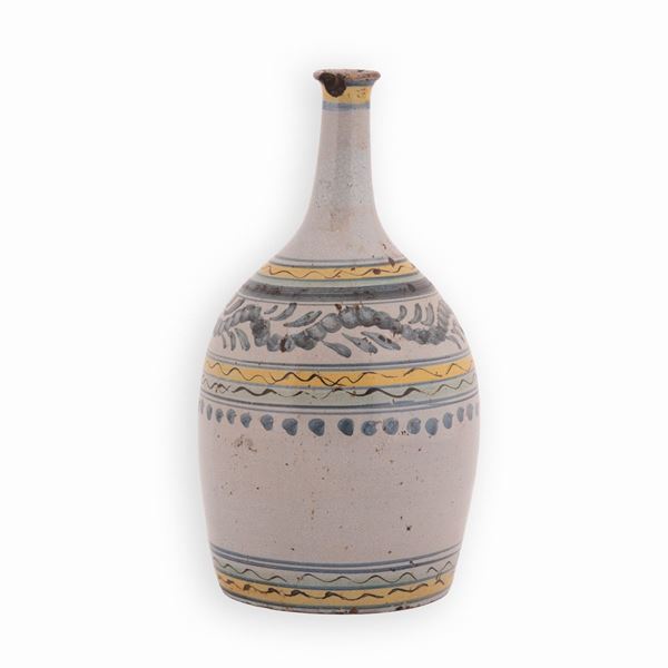 Bottiglia in maiolica a fondo berrettino. Corpo, base e collo decorati con fasce in giallo e blu. Sul corpo festone floreale in blu 