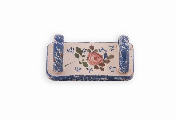 Manifattura castellana del XIX secolo - Schiacciapatate in maiolica policroma. Al centro su fondo bianco decorato con una rosa. Sul doppio manico e sul perimetro motivo in blu realizzato a spugnetta. 