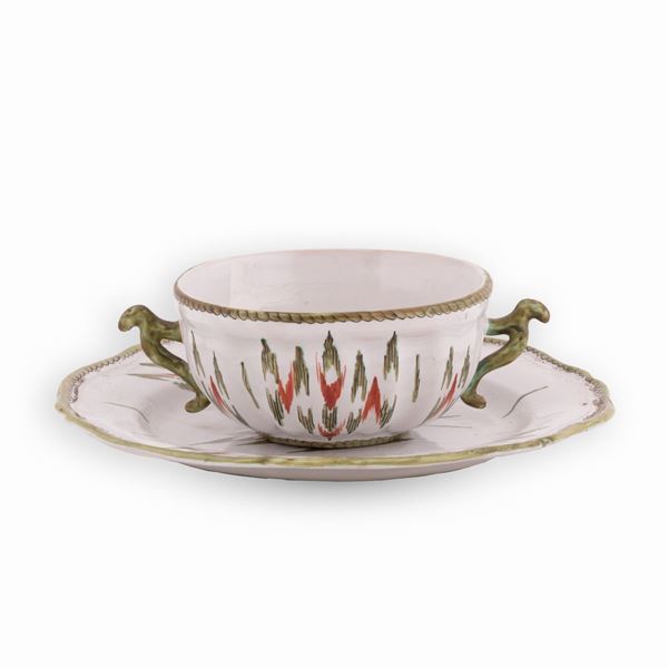 Manifattura dell'Italia del nord del XVIII secolo - Tazza da puerpera in maiolica a doppio manico decorata in policromia a motivi geometrici. Si accompagna ad un piattino dal bordo mistilineo similmente decorato. 