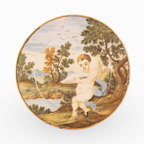 Manifattura castellana del XVIII secolo - Piattino in maiolica decorato in policromia con paesaggio alberato e putto in primo piano. 