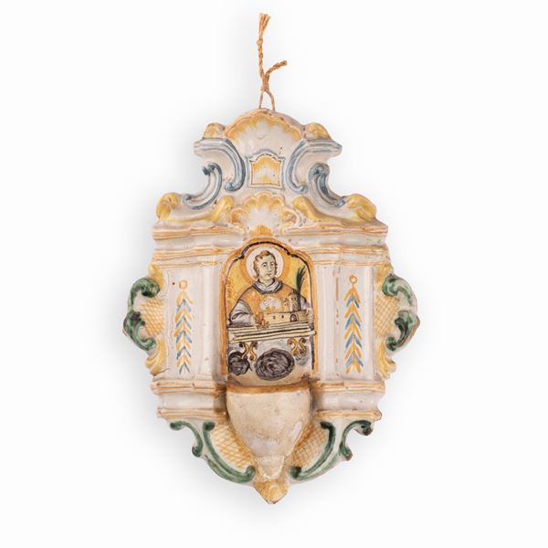 Manifattura castellana della seconda met&#224; del XVIII secolo - Acquasantiera in maiolica decorata con elementi a rilievo e, nell'edicola centrale, con l'effigie di un Santo Martire stante a trattenere un modellino architettonico di una chiesa