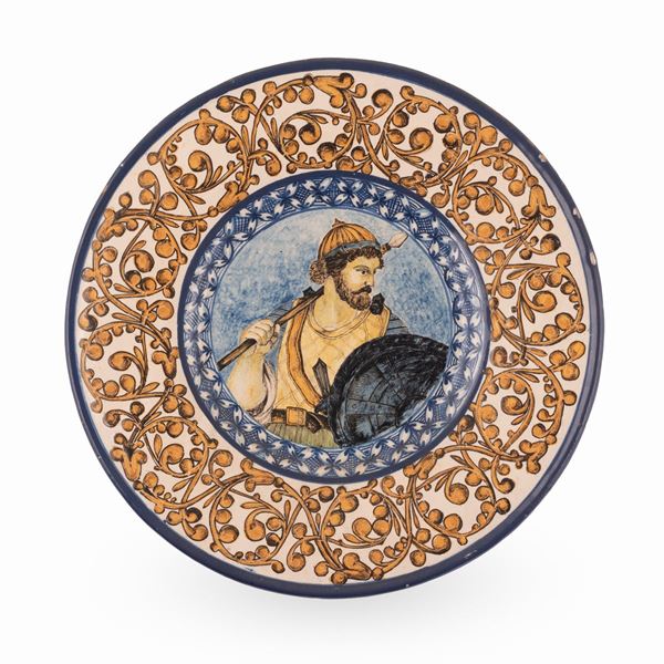 Manifattura dell'Italia centrale dell'ultimo quarto del XIX secolo - Piatto in maiolica decorato sulla tesa con girali fitomorfi e nel cavo, con la figura di un'antico guerriero