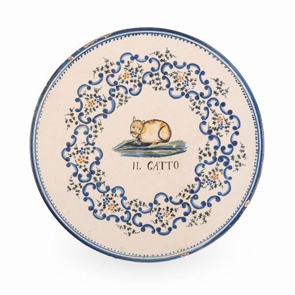 Manifattura abruzzese attiva tra il tardo XIX ed i primi del  XX secolo. - Tagliere in maiolica decorato con la figura di un gatto racchiusa in una riserva circolare, composto da elementi floreali e volute