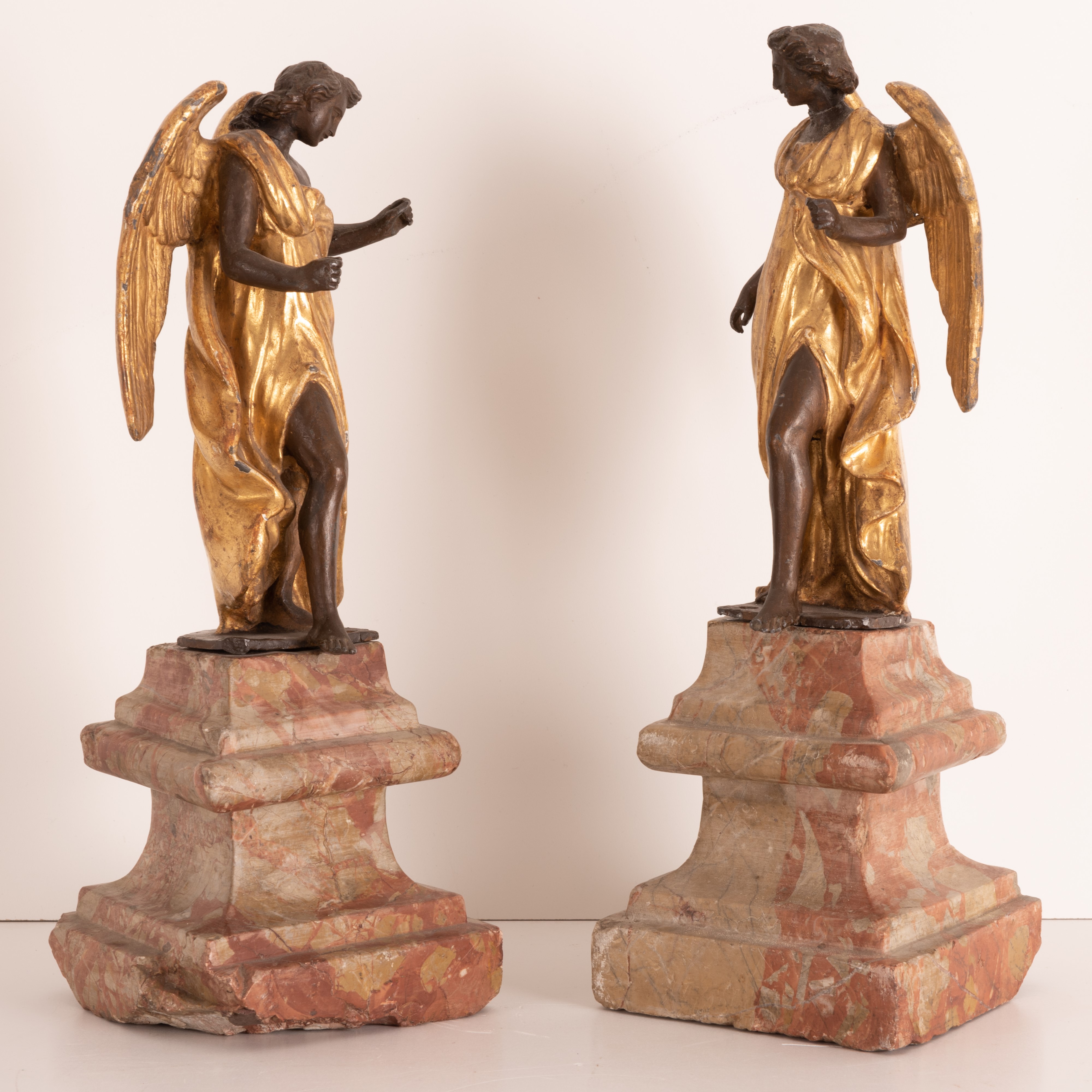 Coppia di sculture in metallo brunito e dorato raffiguranti angeli su antiche basi in marmo