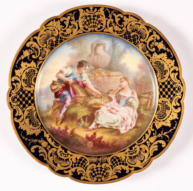 Piatto in porcellana Sevres con tesa a fondo blu e decoro in oro a volute e racemi.