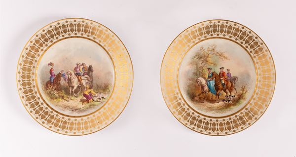 Coppia di piatti in porcellana con decori in oro di gusto secondo ottocento sulla tesa e con al cavetto dipinte scene di caccia. Sevres, fine del XIX inizi - del XX secolo