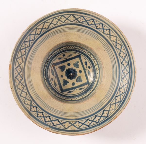 Piatto tondo in maiolica decorato in blu alla tesa con motivo reticolato e puntinato. Al cavetto decoro floreale centrale inquadrato all'esterno con decori fogliati e geometrici.