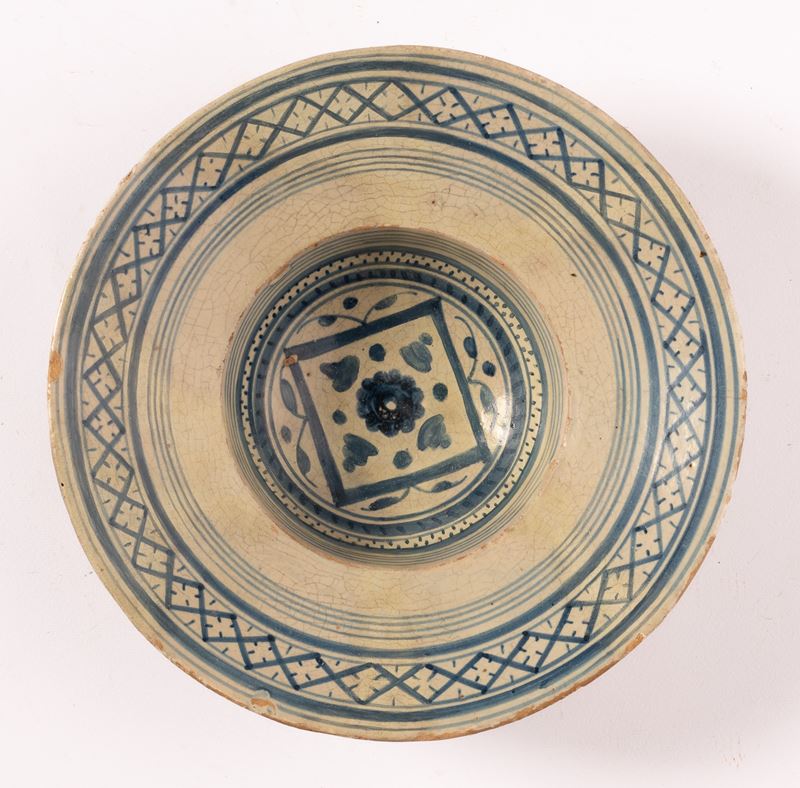 Piatto tondo in maiolica decorato in blu alla tesa con motivo reticolato e puntinato. Al cavetto ...
