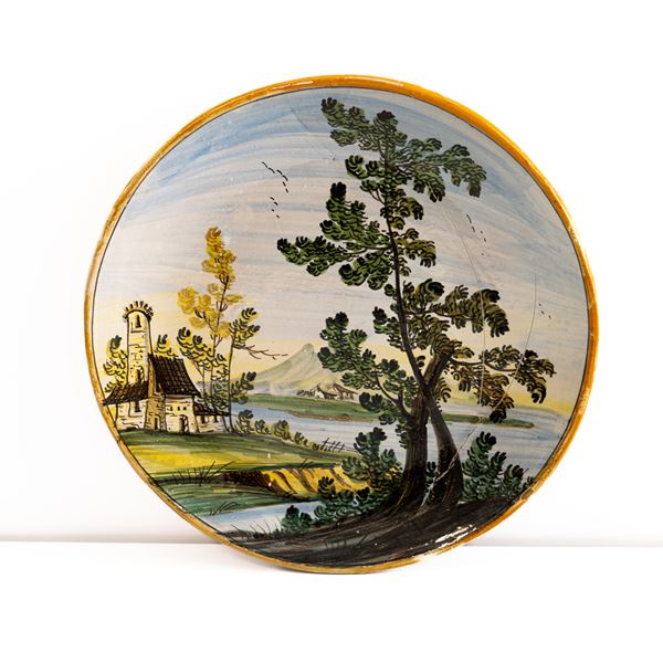 Manifattura di Castelli della met&#224; del XX secolo - Piatto in maiolica con paesaggio fluviale, torre, case e albero 