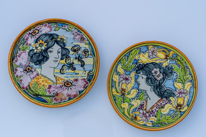 Coppia di piattini Art Nouveau con figure muliebri in serti di fiori e insetti.