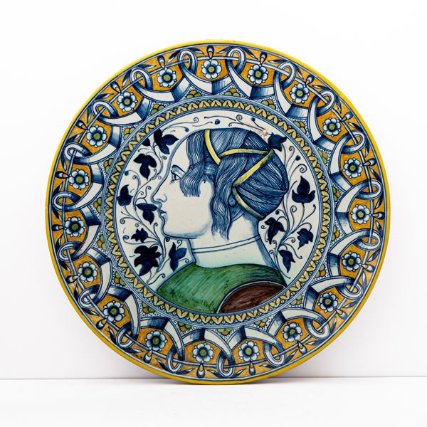 Manifattura Cantagalli del XX secolo - Piatto in maiolica decorato a lustro metallico di gusto liberty. Nella tesa motivo geometrico e floreale intrecciato, nel cavetto figura muliebre di profilo contornata da decoro fogliato