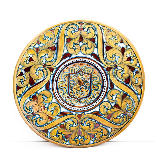 Manifattura di Gualdo Tadino del XX secolo - Piatto in maiolica decorata a lustro metallico con decoro di girali fogliati nella tesa e grifo rampante racchiuso in uno scudo nel cavetto. 