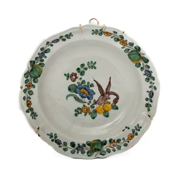 Manifattura di Cerreto Sannita della fine del XVIII secolo - Piatto in maiolica con bordo mistilineo decorato alla tesa con tre composizioni di fiori e frutti e al cavetto con uccello stante su un serto di fiori e frutti