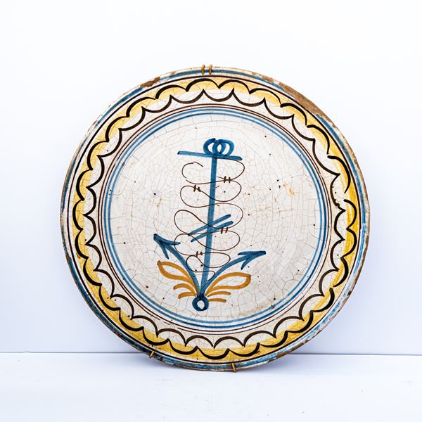 Manifattura campana del XIX secolo - Grande piatto in maiolica con decoro a treccia in manganese sulla tesa e disegno stilizzato di un'ancora in azzurro e arancio nel cavo 